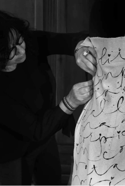 Fotografia in bianco e nero di Dolores Mauro mentre lavora a mano su un abito decorato con scritte