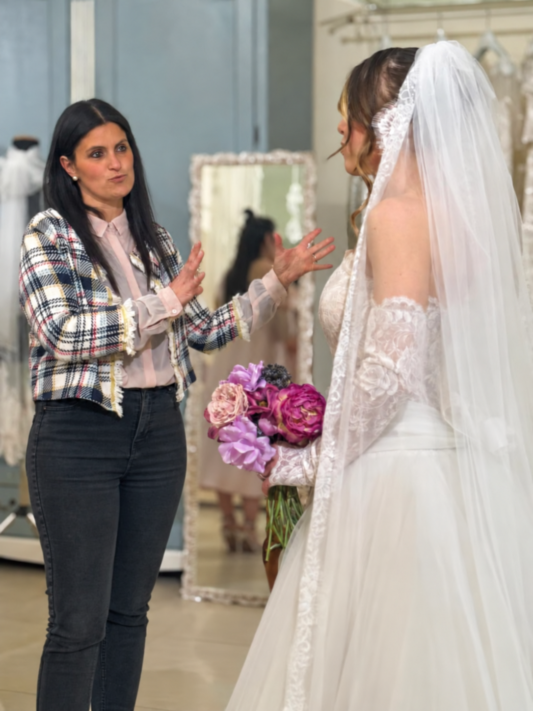 Consulenza in atelier a una sposa con velo, abito in pizzo e bouquet rosa e viola